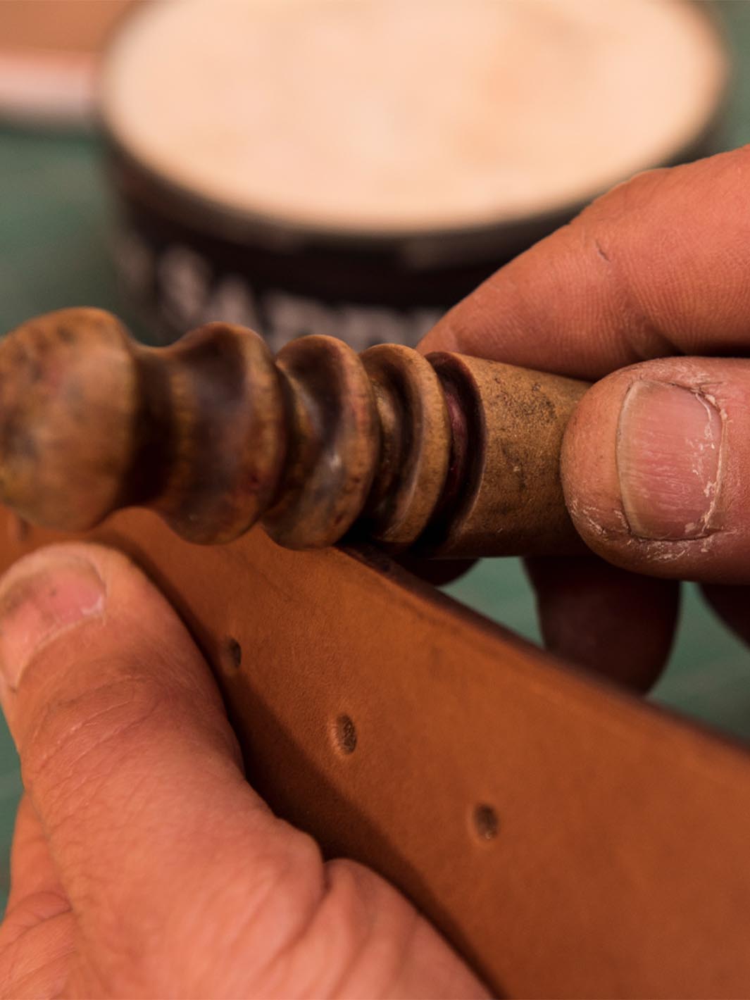 mani di un artigiano che rifiniscono i bordi di una cintura in cuoio per uomo