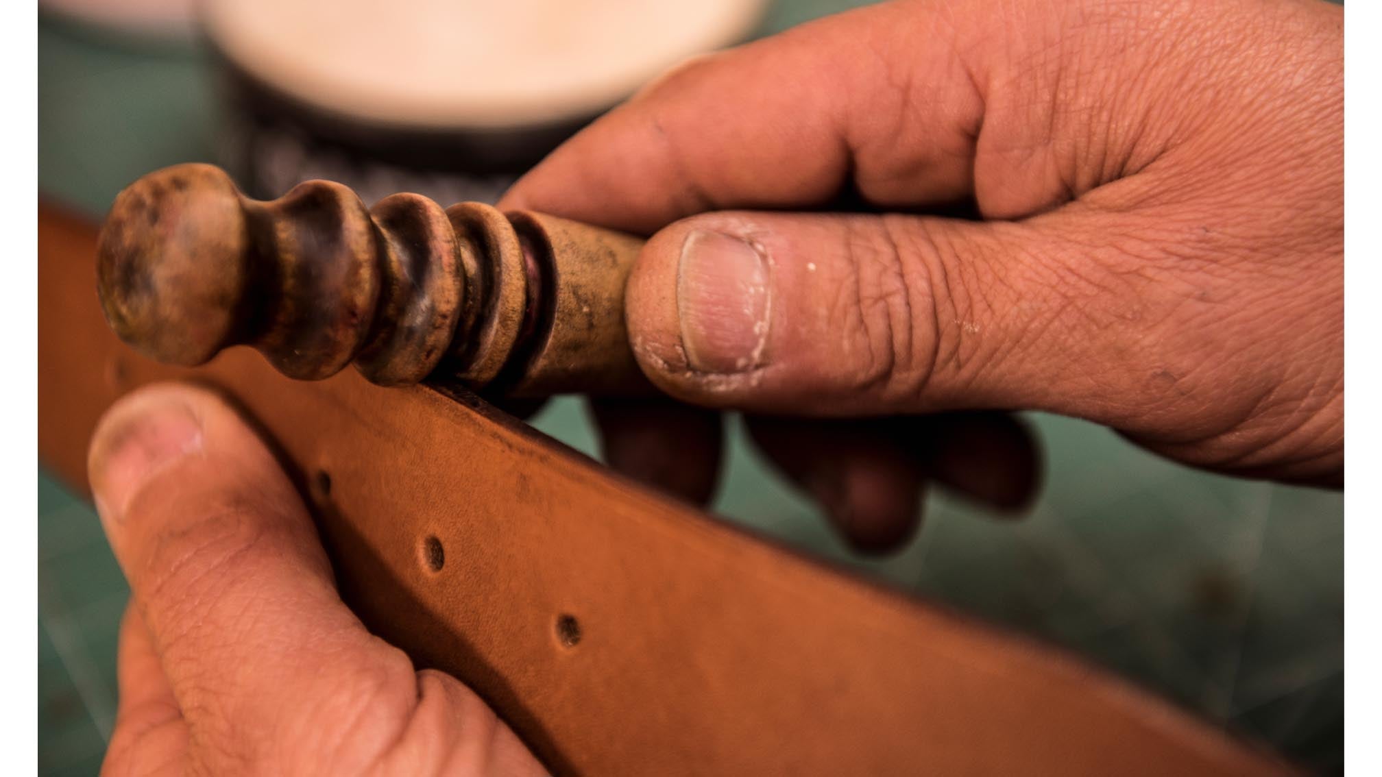 mani di un artigiano che rifiniscono i bordi di una cintura in cuoio per uomo
